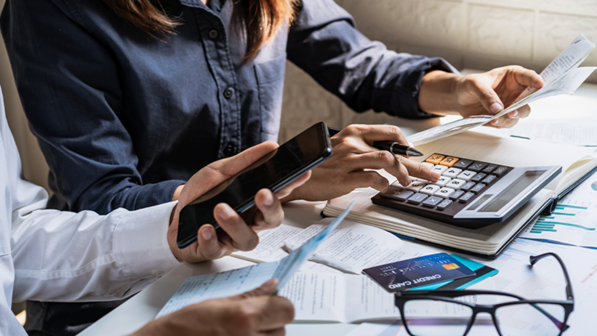 A imagem de pessoas analisando contas com calculadora e cartões de crédito ilustra o serviço de defesa em ações bancárias para Pessoa Jurídica.