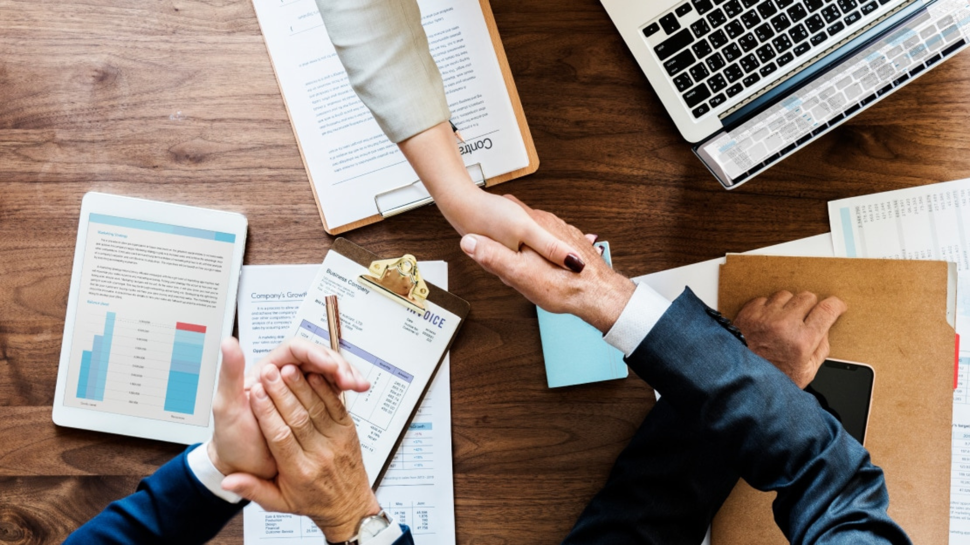 A imagem de um aperto de mãos em mesa com documentos e computador ilustra o serviço de negociação de dívidas para Pessoa Jurídica em direito bancário.